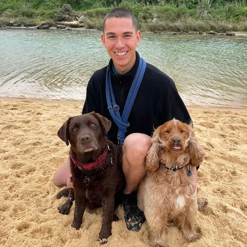 Selwyn, professional dog walker at Stellar Paws, with two happy dogs during an off-leash beach walking session in Sydney